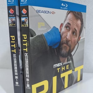 May include: Two Blu-ray disc cases for "The Pitt" season 1 and 2. The cases are blue and black with the show's title in large yellow letters. The cover features a man in medical attire. The text "National Doctors Day" is also visible.