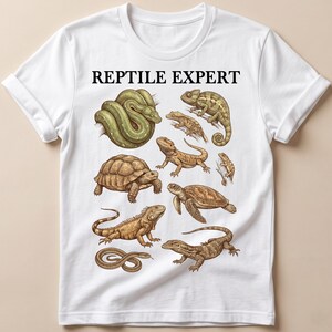 May include: A white short-sleeved t-shirt featuring the black text REPTILE EXPERT at the top. Below the text are detailed illustrations of various reptiles including a green snake, a chameleon, a tortoise, a lizard, a sea turtle, and an iguana.