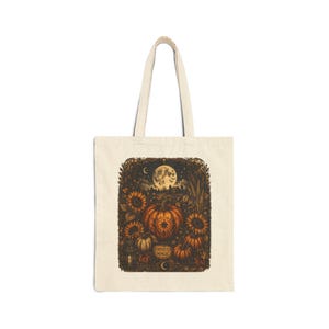Peut inclure: Un sac fourre-tout beige orné d'une illustration sombre et détaillée représentant une grosse citrouille orange, des tournesols et une pleine lune brillante. Le motif inclut une lanterne, des petites citrouilles et le texte Harvest The Magic.