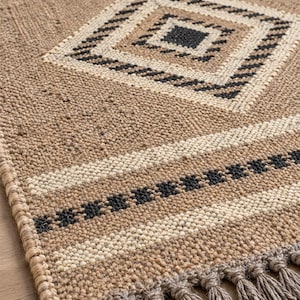 May include: A rectangular woven rug featuring a natural tan jute base with a repeating diamond pattern in cream and black. The rug includes horizontal striped bands in cream and black near the edge, finished with a row of knotted jute tassels.