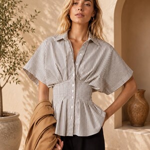 May include: A short-sleeved button-down shirt featuring a vertical brown and white striped pattern, a classic collar, and a cinched waist design that creates a peplum silhouette. The shirt is paired with solid black trousers and a tan jacket.