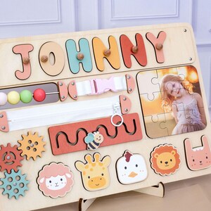 May include: Wooden activity board with the name "JOHNNY" in colorful letters. Features include a zipper, buckle, bead maze, gears, and animal-shaped puzzle pieces. A photo puzzle is also included.