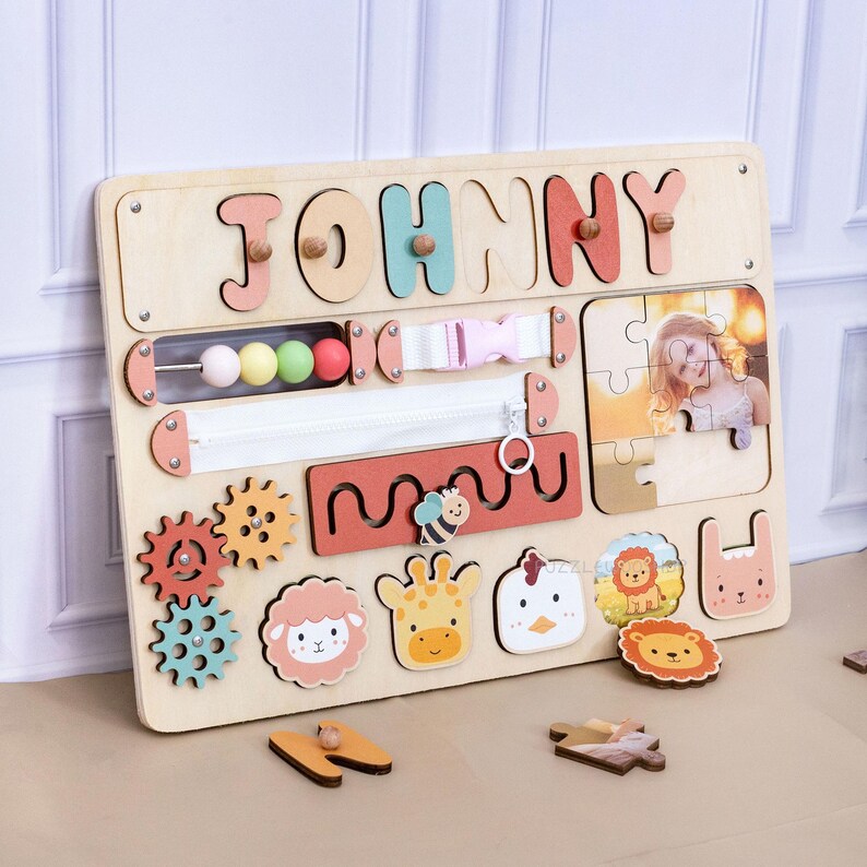May include: Wooden activity board with the name "JOHNNY" in colorful letters. Features include a zipper, buckle, bead maze, gears, animal shapes, and a photo puzzle. The board is designed for early childhood development and learning.