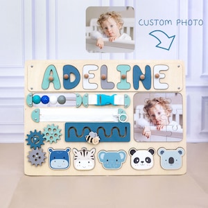 May include: Wooden busy board with the name "ADELINE" in blue and teal letters. Features include a zipper, buckle, gears, and animal shapes. Includes a custom photo and puzzle.