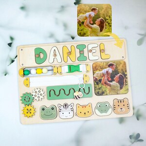 May include: Wooden activity board with the name "DANIEL" in yellow and green letters. Features include a puzzle, gears, beads, a buckle, a zipper, and animal shapes. Includes a photo of a mother and child.