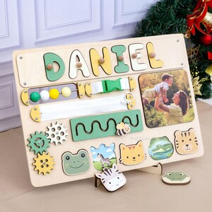 May include: Wooden activity board with the name "DANIEL" in colorful letters. Features include a zipper, buckle, gears, beads, and animal-shaped puzzle pieces. A photo of a mother and child is also included.