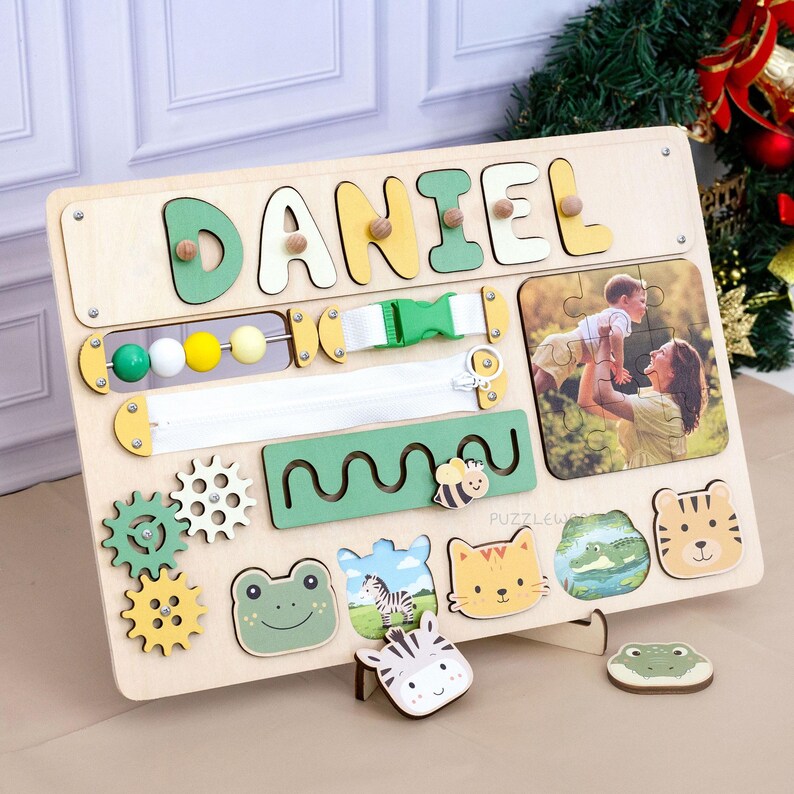 May include: Wooden activity board with the name "DANIEL" in colorful letters. Features include a zipper, buckle, gears, beads, and animal-shaped puzzle pieces. A photo of a mother and child is also included.