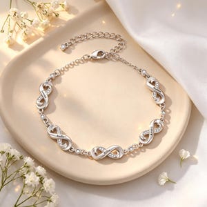 Puede incluir: Una pulsera de cadena plateada con cuatro eslabones en forma de símbolo de infinito, cada uno decorado con pequeñas piedras transparentes y grabado con los nombres Lucas, Sadler, Riley y Averil. Incluye un cierre de mosquetón y cadena ajustable.