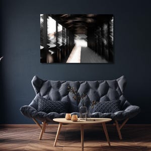 May include: A black and white abstract art print depicting a long hallway with a bright light at the end. The artwork is displayed above a gray tufted sofa with decorative pillows and a wooden coffee table.