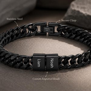 Könnte beinhalten: Ein schwarzes Edelstahl-Armband mit Panzerkette und sicherem Verschluss. Das Armband verfügt über individuell gravierte Perlen mit den Namen "Liam" und "Noah". Der Text "Stainless Steel" ist auf dem Verschluss sichtbar.