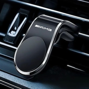 Könnte beinhalten: Eine schwarze magnetische Autohalterung für Mobiltelefone mit silbernem Rand und dem in Weiß aufgedruckten AMG-Logo. Die Halterung verfügt über eine kreisförmige Magnetfläche und einen Clip zur Befestigung an den Lamellen der Lüftung.