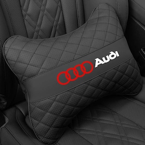 Può includere: Un cuscino poggiatesta per auto nero con motivo trapuntato a rombi e texture traforata. Una fascia orizzontale al centro mostra il logo Audi con quattro anelli rossi e il nome del marchio Audi in bianco con un carattere sans-serif pulito.