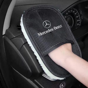 Op de afbeelding: Een zwarte reinigingshandschoen met een witte pluche onderkant en een mesh bovenkant met het Mercedes-Benz logo en de tekst in het wit. De handschoen is ontworpen voor auto-onderhoud en biedt een zacht oppervlak voor het reinigen van interieurs.