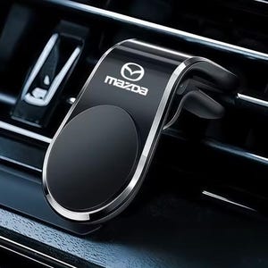 May include: A black magnetic car phone mount with a silver trim and the Mazda logo printed in white. The device features a circular mounting surface and a clip mechanism designed to attach securely to a vehicle's horizontal air conditioning vent.