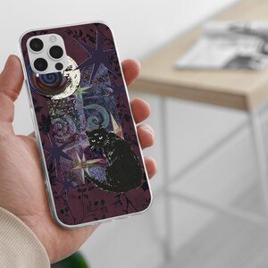 May include: A clear phone case featuring a dark purple background with a black cat illustration, a crescent moon with a face, and various star shapes. The design includes intricate swirling patterns and botanical silhouettes in deep shades of purple.