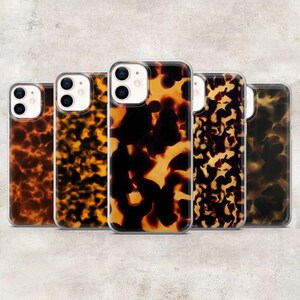May include: Five phone cases with a tortoiseshell pattern in shades of brown, black, and yellow. The cases have a clear border and are designed for a smartphone. The cases are arranged in a row, showcasing the variety of patterns.