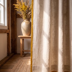 Op de afbeelding: Een kamerhoog gordijn van lichtbeige, gestructureerde stof met een verticale mosterdgele rand aan de zijkant en een horizontale mosterdgele band langs de onderzoom, wat een duidelijk contrast vormt met het neutrale materiaal.