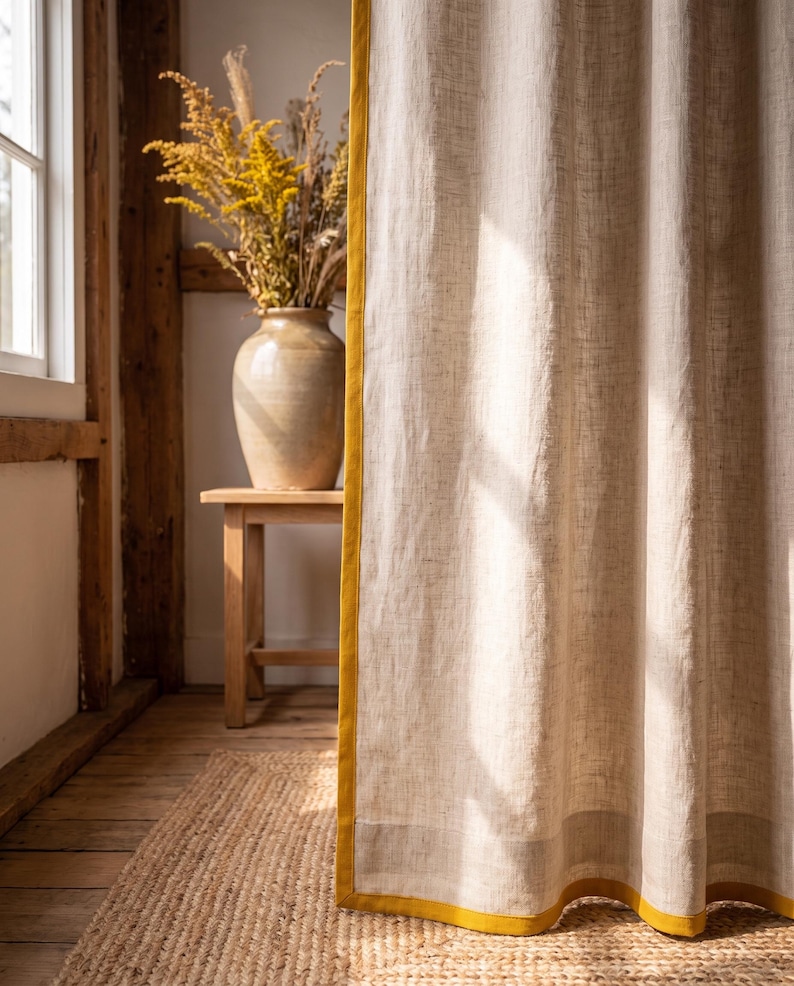 Op de afbeelding: Een kamerhoog gordijn van lichtbeige, gestructureerde stof met een verticale mosterdgele rand aan de zijkant en een horizontale mosterdgele band langs de onderzoom, wat een duidelijk contrast vormt met het neutrale materiaal.