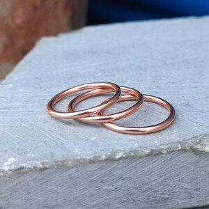 May include: Three thin, polished copper rings with a smooth, rounded surface. The rings are arranged in a slightly overlapping, stacked formation, showcasing their metallic, reddish-brown hue and simple, circular design without any added embellishments.