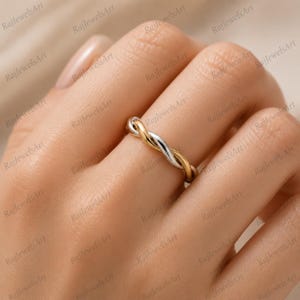 Pode incluir: Um anel de dois tons com um design torcido, apresentando uma banda em ouro amarelo polido e outra em prata polida. Os fios de metal estão entrelaçados para criar um padrão contínuo semelhante a uma corda que envolve o dedo.