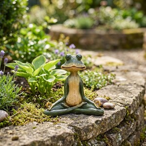 K&ouml;nnte beinhalten: Eine gr&uuml;n-beige Froschfigur in sitzender Meditationshaltung mit geschlossenen Augen und auf den Knien ruhenden H&auml;nden. Der Frosch hat ein glattes, geschnitztes Aussehen mit hellem Bauch und dunkelgr&uuml;nen Gliedma&szlig;en in Schneidersitz.