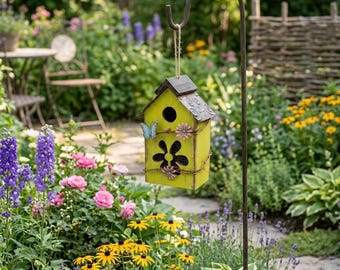 May include: A yellow birdhouse with a dark grey roof and flower cutouts hangs from a metal hook in a garden. The birdhouse is decorated with a butterfly and floral accents. The garden features colourful flowers and greenery.