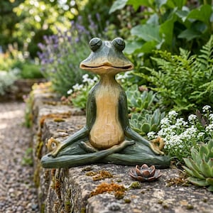 K&ouml;nnte beinhalten: Eine gr&uuml;n-beige Froschfigur in sitzender Meditationshaltung mit geschlossenen Augen und H&auml;nden in Mudra-Position. Der Frosch hat ein glattes, geschnitztes Aussehen mit hellem Bauch und dunkelgr&uuml;nen Gliedma&szlig;en, platziert neben einer kleinen Lotusbl&uuml;te.