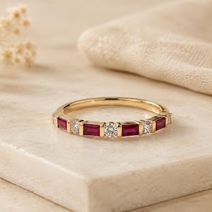 Op de afbeelding: Een gouden ring met een afwisselend patroon van rechthoekig geslepen rode robijnen en rond geslepen witte diamanten in een kanaalzetting. De ring heeft een gepolijste gouden afwerking met een symmetrisch ontwerp van edelstenen.