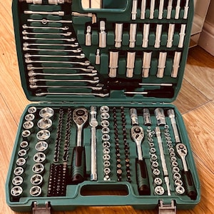 Pode incluir: Um conjunto completo de ferramentas alojado numa mala de transporte de plástico verde-azulado. O kit inclui vários componentes de metal prateado, tais como chaves de caixa, chaves de vários tamanhos, chaves combinadas e pontas de aparafusar.