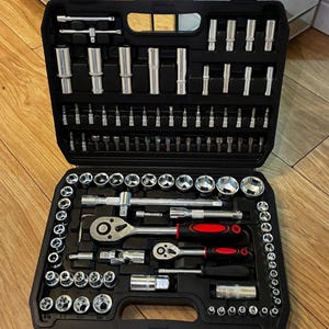 May include: A comprehensive black plastic tool case containing a wide assortment of silver metal socket wrench components, including various sized sockets, two ratchets with black and red handles, extension bars, and multiple screwdriver bits.