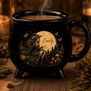 May include: A black ceramic cauldron-shaped mug with a handle and three feet. The front features a graphic of a person in a green cloak and hat riding a broomstick in front of a large yellow moon, with the name Emily printed in script.
