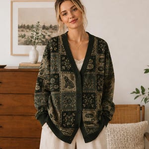 May include: A dark green and olive V-neck cardigan featuring a patchwork design of botanical illustrations and a frog graphic. The knit garment has a button-down front closure, long sleeves with ribbed cuffs, and a repeating pattern of flowers.