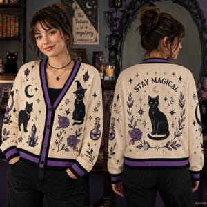 May include: A cream-colored button-up cardigan featuring purple and black graphics of a cat wearing a witch hat, roses, crystals, and potion bottles. The back displays a cat illustration with the text "STAY MAGICAL" and purple trim.