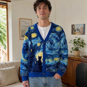 May include: A blue V-neck cardigan featuring a printed pattern inspired by The Starry Night, including swirling yellow stars, a dark silhouette of a cat, and a solid blue trim with four brown buttons, worn over a plain white t-shirt.