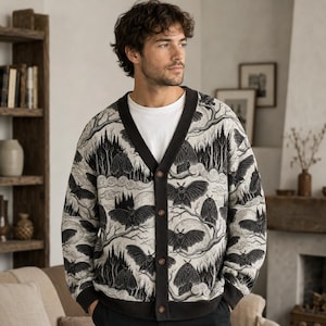 Peut inclure: Un cardigan boutonné à manches longues avec un imprimé graphique noir et blanc représentant des papillons de nuit, des branches d'arbres dénudées et des lunes. Il présente un col en V, des poignets et un ourlet noirs, porté sur un t-shirt blanc.