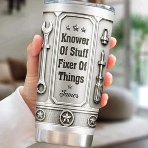 May include: A silver-toned stainless steel tumbler featuring a metallic texture with a central panel displaying the text "Knower Of Stuff Fixer Of Things" and the name "James". The design includes illustrations of a wrench, a screwdriver, and stars.