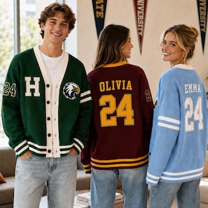 May include: Three varsity-style cardigans in green, maroon, and light blue. The green cardigan features a white H, an eagle emblem, and the number 24. The maroon cardigan displays the name OLIVIA and 24. The light blue cardigan shows EMMA and 24.