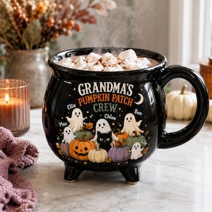 Può includere: Una tazza in ceramica nera a forma di calderone con un disegno di fantasmi, zucche e un gatto nero. Il testo recita "GRANDMA'S PUMPKIN PATCH CREW" con i nomi "Ellie", "Max", "Chloe", "Ben" e "Lily". La tazza è dotata di tre piedini.