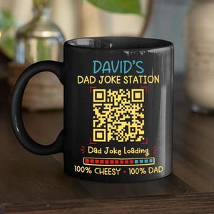 May include: A black ceramic mug featuring the text DAVID'S DAD JOKE STATION in blue and yellow, a yellow QR code, the text Dad Joke Loading, a progress bar with red and blue segments, and the text 100% CHEESY 100% DAD in yellow and white.