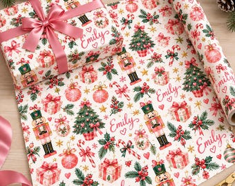 Puede incluir: Un rollo de papel de regalo blanco con un patrón repetitivo de cascanueces, árboles de Navidad, cajas de regalo, bastones de caramelo y acebo, con el nombre Emily y corazones pequeños impresos en letra cursiva rosa.