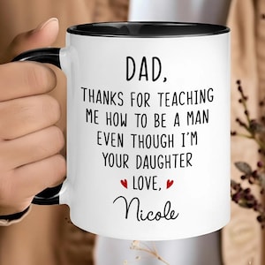 May include: White ceramic mug with a black interior and handle. The mug features the text "DAD, THANKS FOR TEACHING ME HOW TO BE A MAN EVEN THOUGH I'M YOUR DAUGHTER LOVE, Nicole" in black font with red hearts.