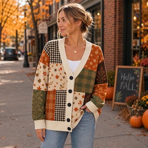 May include: A long-sleeve button-down cardigan featuring a patchwork design with various autumn-themed patterns including maple leaves, plaid, and gingham in shades of orange, brown, cream, and olive green, finished with a cream-colored V-neck trim.
