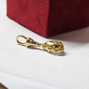 May include: A gold pendant featuring a teardrop-shaped clear gemstone set in a metal frame with a decorative openwork gallery. The pendant includes a polished gold bail at the top, designed for attachment to a chain or necklace for jewelry wear.