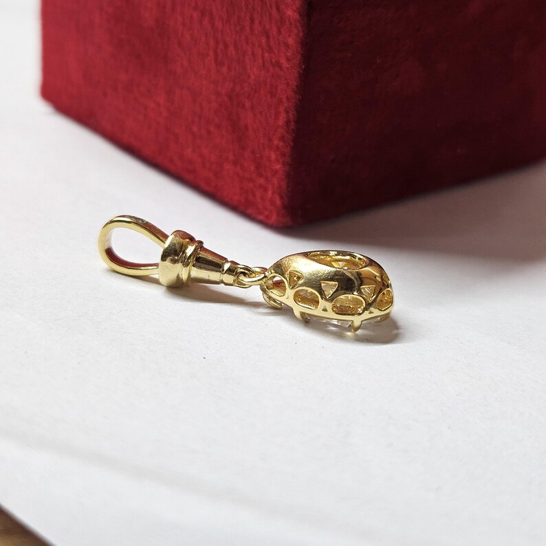 May include: A gold pendant featuring a teardrop-shaped clear gemstone set in a metal frame with a decorative openwork gallery. The pendant includes a polished gold bail at the top, designed for attachment to a chain or necklace for jewelry wear.