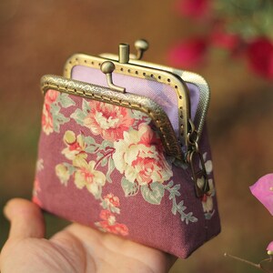 Op de afbeelding: Een kleine paarse bloemen portemonnee met een gouden metalen frame en een ritssluiting.