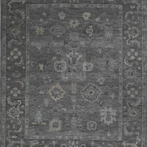 May include: A rectangular area rug in dark charcoal gray featuring a repeating pattern of light gray floral and geometric motifs. The rug has a wide decorative border with intricate scrollwork and symmetrical shapes surrounding a central field.
