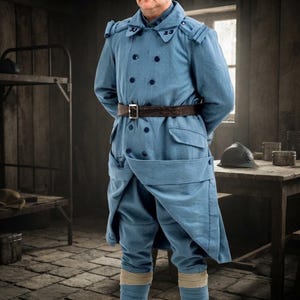 Op de afbeelding: Een lichtblauwe dubbelrijige militaire overjas met donkerblauwe knopen, een bruine leren riem met metalen gesp en een bijpassende lichtblauwe broek met beige beenwindsels. De kraag is voorzien van kleine, donkerblauw geborduurde cijfers.