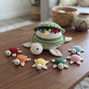 May include: A large crocheted turtle container with a removable green shell lid, filled with small colorful crocheted balls. Six smaller crocheted turtles in red, orange, yellow, green, pink, and blue are arranged in a semi-circle around the main turtle.