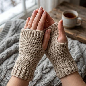 May include: A pair of beige fingerless gloves crafted with a textured crochet stitch. The gloves feature a ribbed cuff at the wrist and a separate opening for the thumb, providing a snug fit that covers the palm while leaving the fingers exposed.