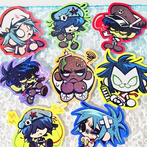 Puede incluir: Un conjunto de ocho pegatinas de vinilo con purpurina que muestran personajes de dibujos animados estilizados con colores de pelo vibrantes, incluyendo azul, verde y negro, con varios sombreros y accesorios, con el texto 8 pcs!! en la esquina inferior derecha.